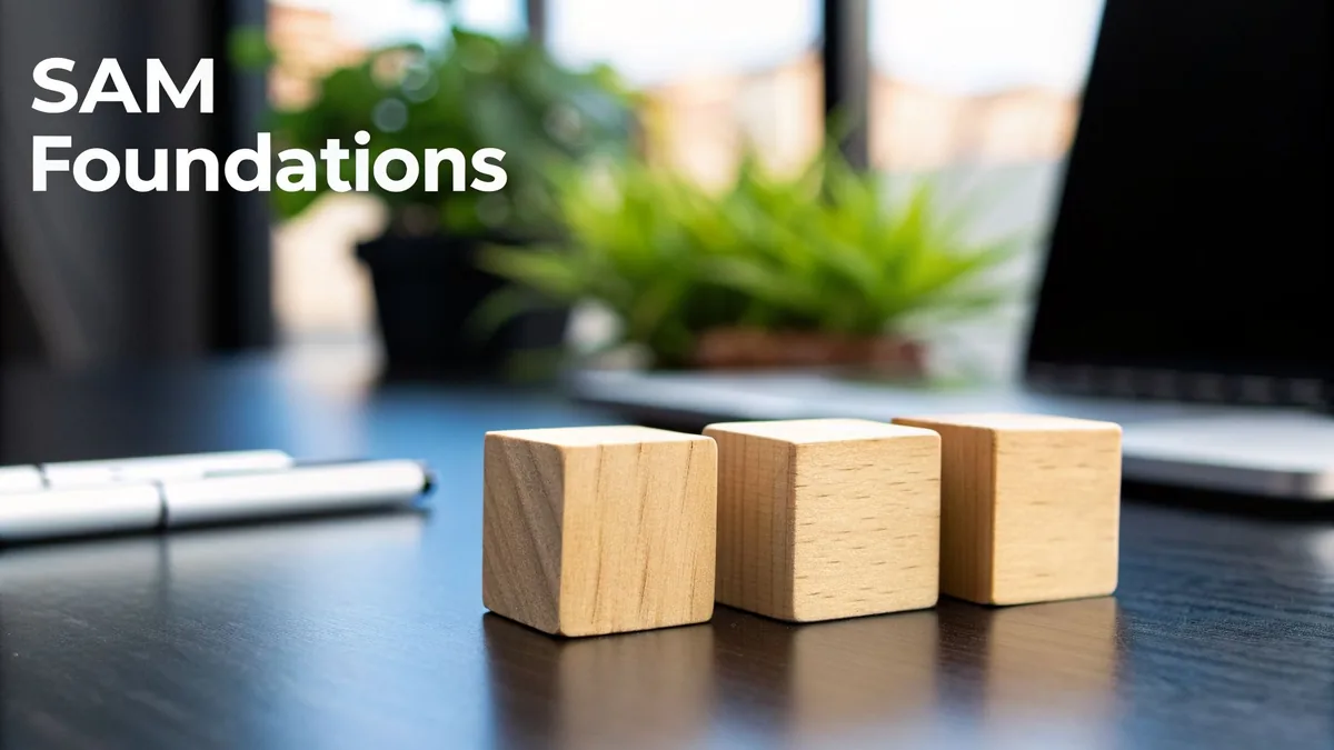 White text 'SAM Foundations' on a blurred desk with wooden blocks, pens, and a laptop.